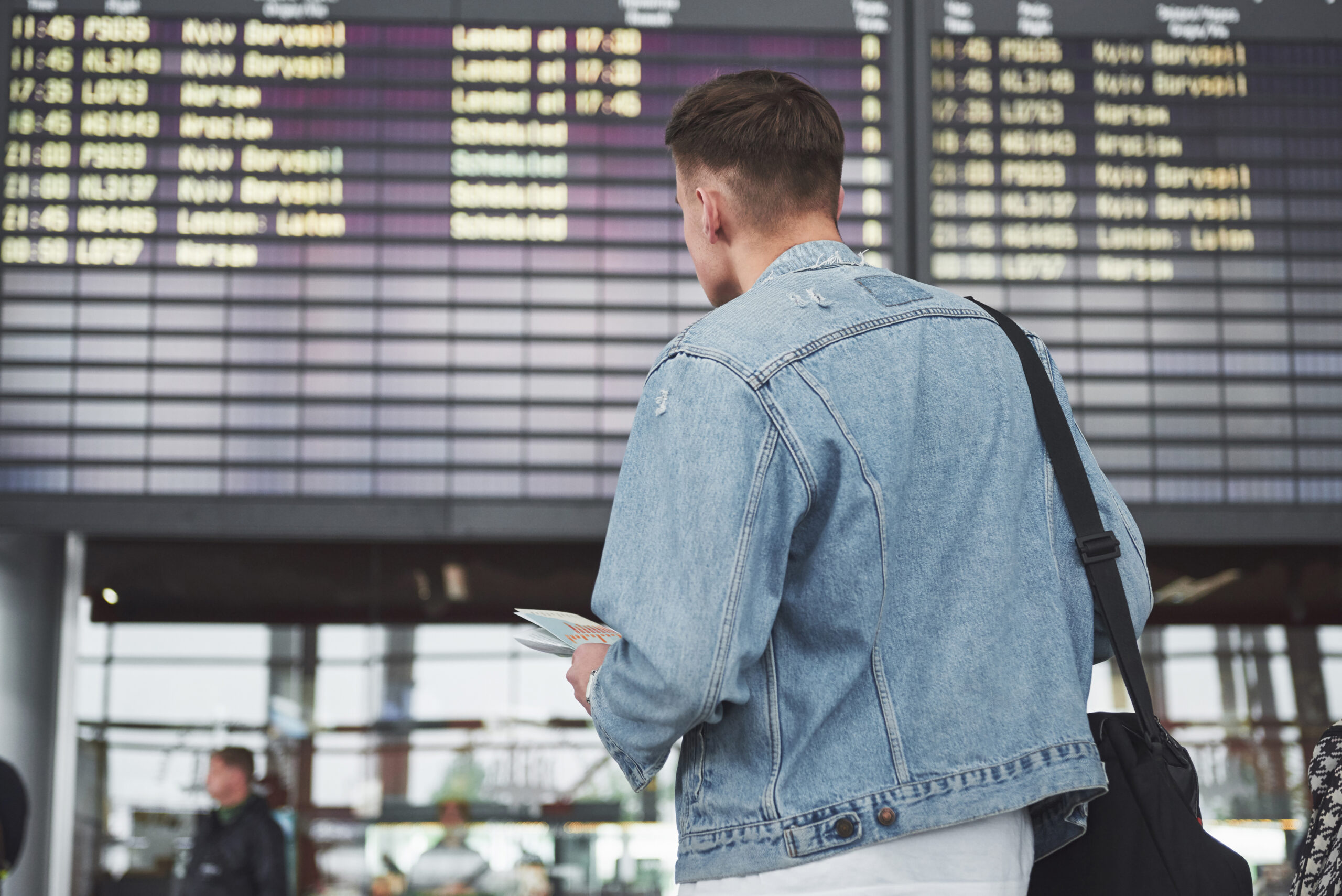Um homem esperando por seu voo no aeroporto na frente de uma tela.