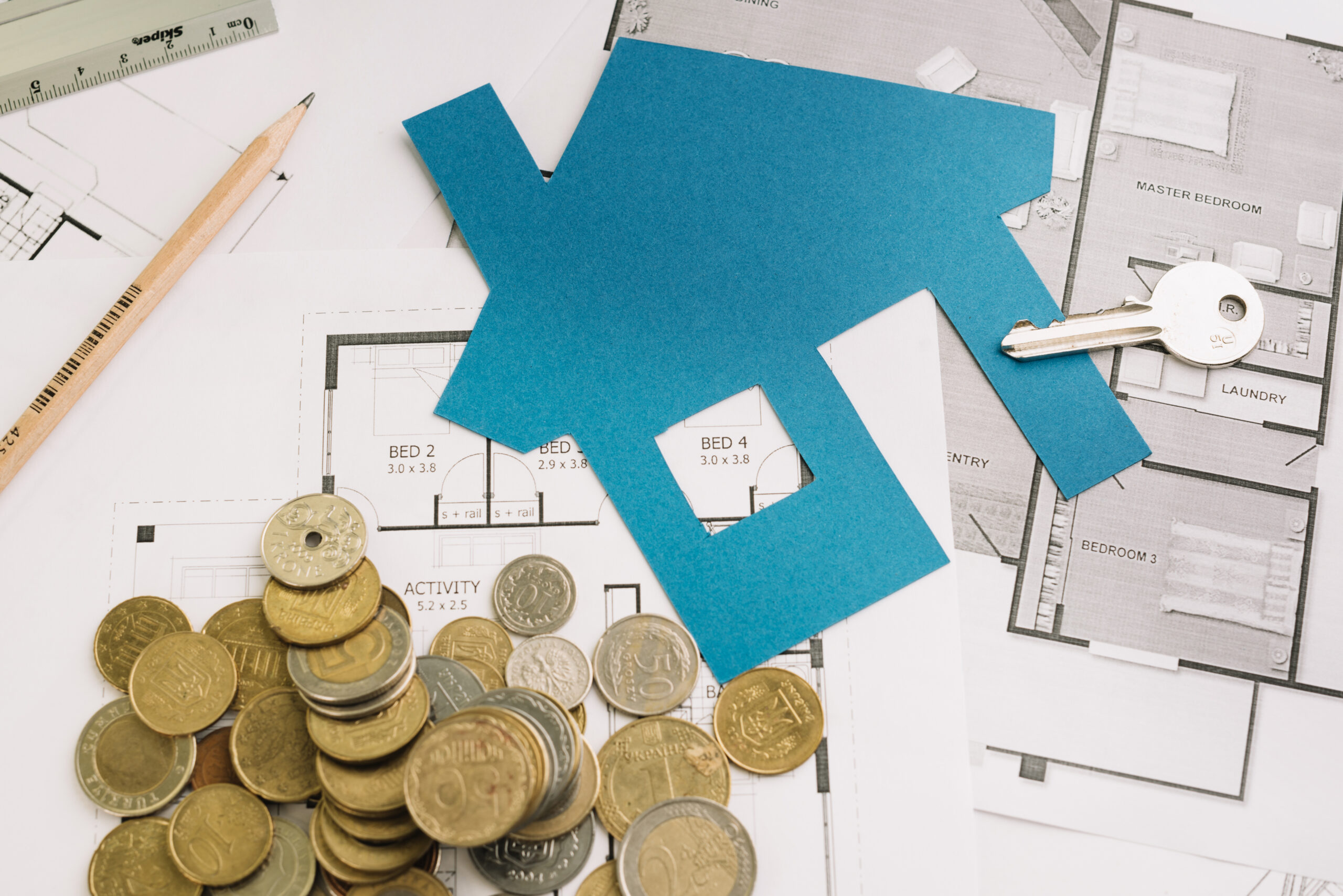 Imagem de uma mesa com várias folhas de plantas de casas, moedas e um papel cortado em azul ao lado de uma chave. Essa imagem ilustrado o blogo com tema "home equity para fintechs e bancos"