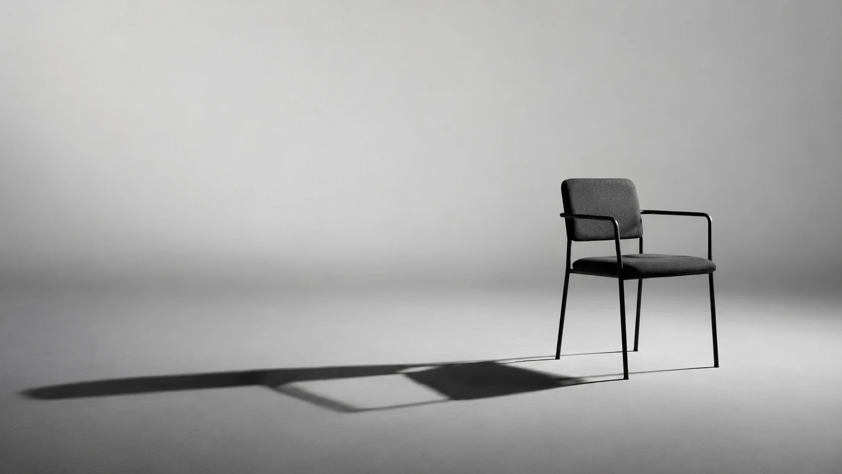 Cadeira de design minimalista, com estrutura metálica preta e assento estofado cinza escuro, em fundo neutro com sombra projetada no piso.